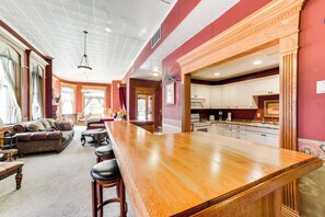Een ruime woonkamer met een houten bar en zithoek, een keuken met witte kasten, en een rode accentmuur.