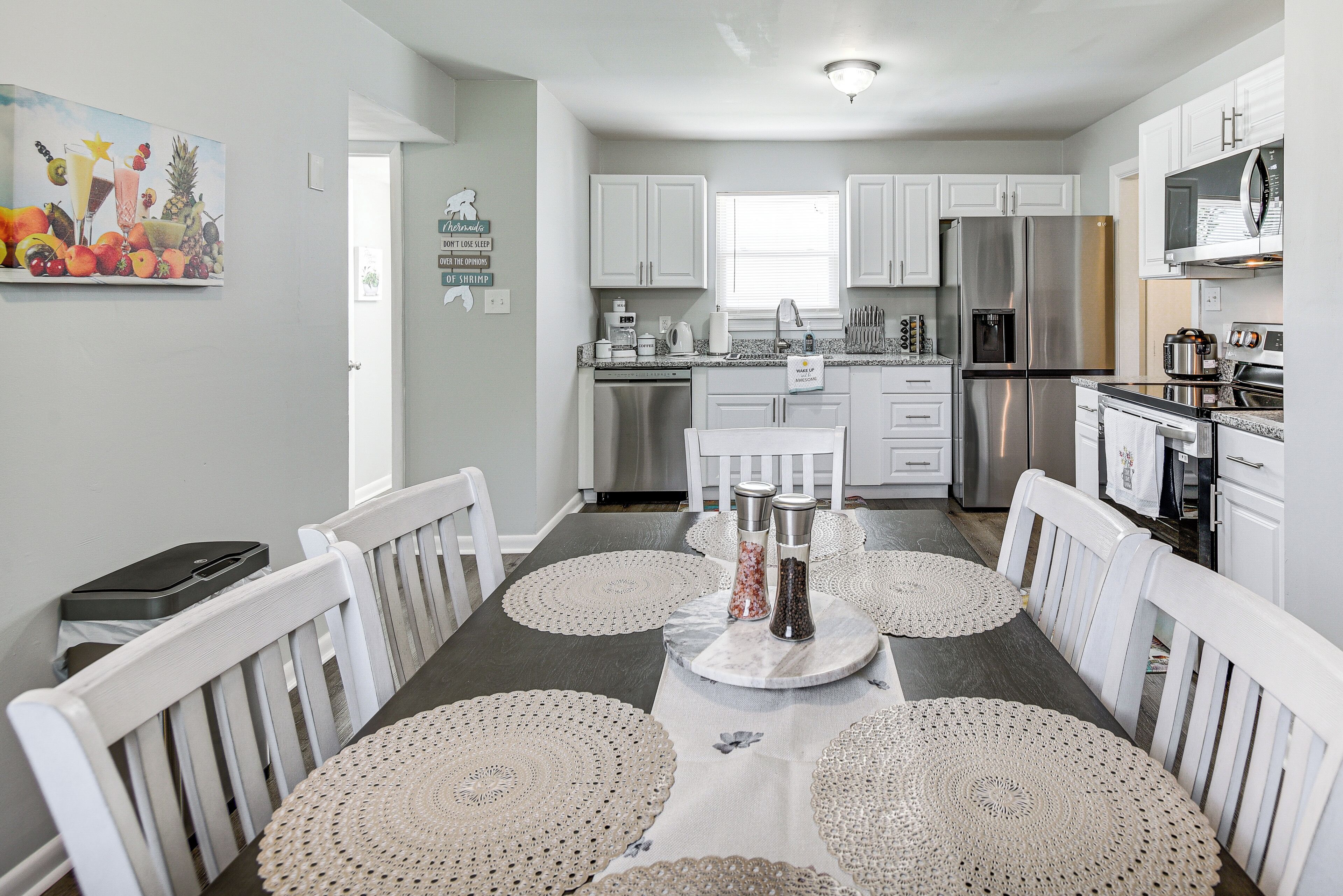 A modern kitchen with white cabinets, stainless steel appliances, and a dining area with white chairs and a table set with doilies.