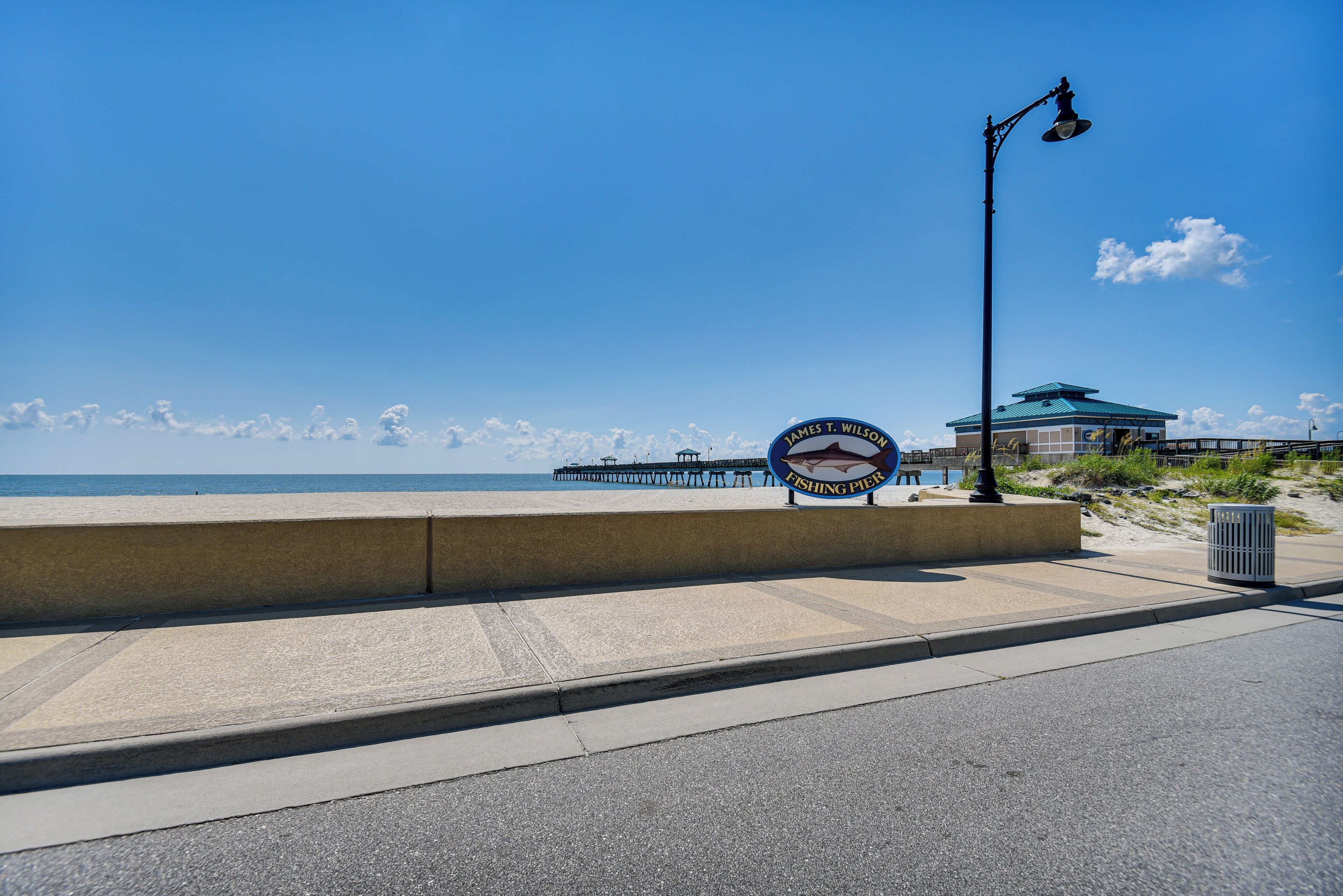 A coastal walkway with a sign reading "James T. Wilson Fishing Pier" and a pier in the background.