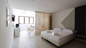Une chambre d’hôtel moderne, dotée d’un grand lit, d’un bureau et d’une chaise. Une fenêtre laisse entrer la lumière naturelle et offre une vue sur l’extérieur.