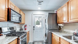 A kitchen with wooden cabinets, a stainless steel microwave, a gas stove, a washing machine, and a refrigerator. - 2 Blocks to Beach: Apt w/ Grill in Ocean Gate! (Ocean Gate)