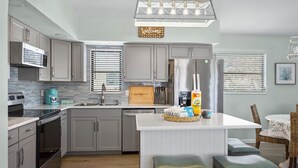 A modern kitchen with grey cabinets, a central island with stools, a built-in oven, and a coffee maker. - 🌊Pet Friendly-Walk to Beach-Sea Salt Escape🌊 (Fort Myers Beach)