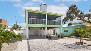 A two-story building with a green and white color scheme, a covered outdoor area, and a small garden with palm trees. - 🌊Pet Friendly-Walk to Beach-Sea Salt Escape🌊 (Fort Myers Beach)