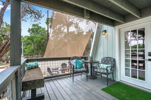 Une terrasse extérieure couverte, avec un banc en bois, deux chaises avec des coussins, une petite table et un foyer.