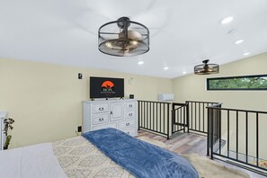 Une chambre moderne avec un lit, une commode, un téléviseur et un balcon doté d’une balustrade.