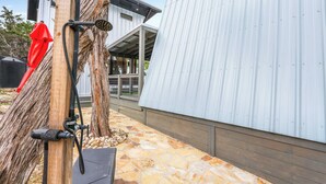 A modern building with a sloped metal roof, a stone-paved patio, and a wooden post with a hose and showerhead.