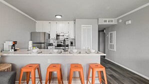 A modern kitchen with white cabinets, stainless steel appliances, and a bar area with orange stools. - New Heated Pool & Hot tub! Escape Here! (Galveston)