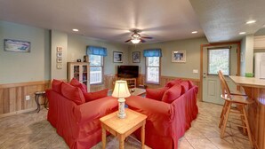 A living room with a red sofa set, a wooden coffee table, a television, and a ceiling fan. - Diamond In The Rough: Rooftop Deck | Rec Room (Ocracoke)