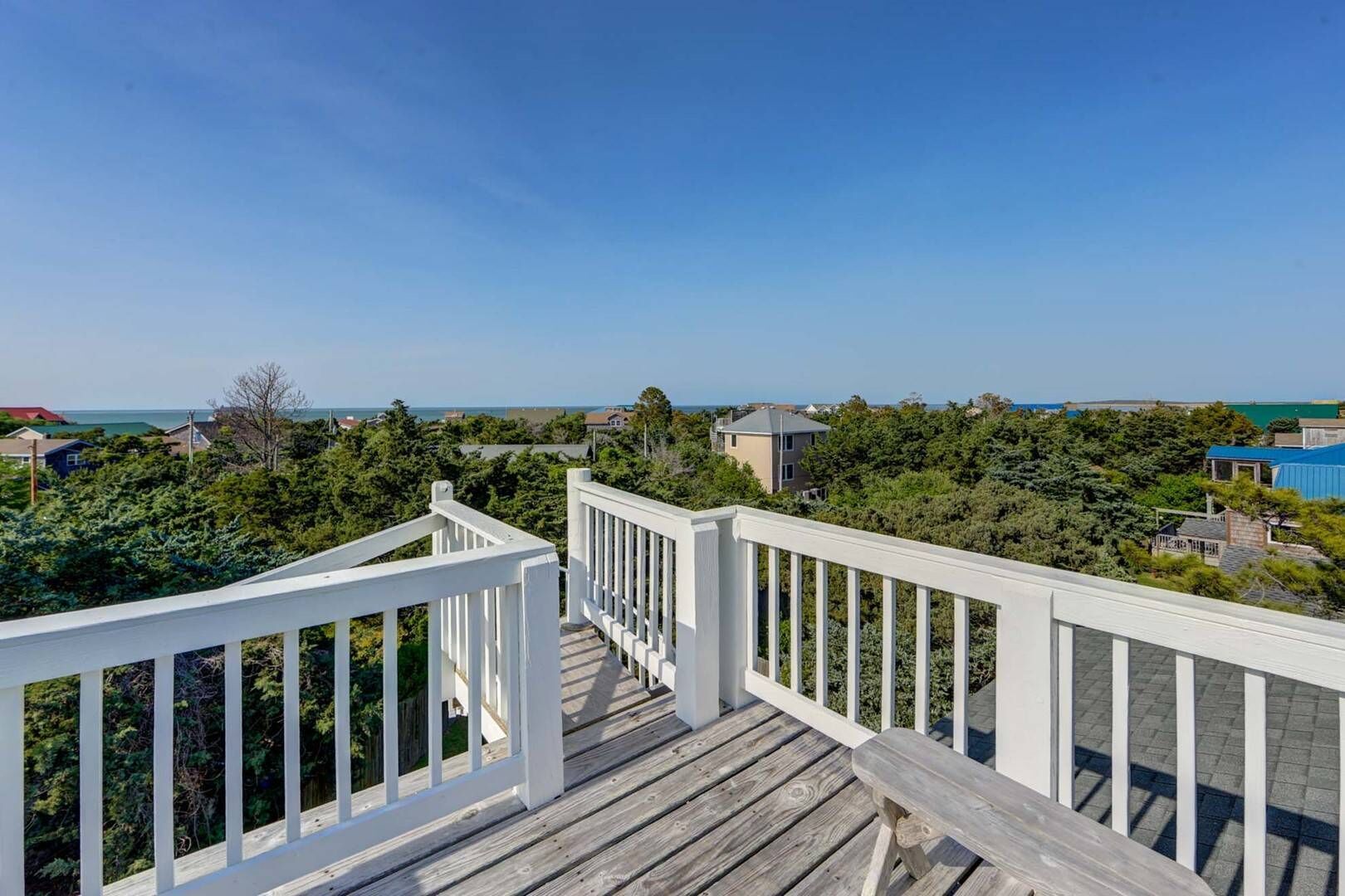 A wooden deck with white railings overlooking a coastal area with houses and greenery.