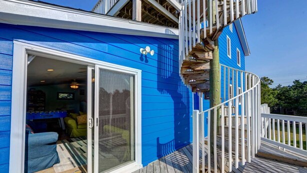 A blue building with a glass door leading to a room with a foosball table and a yellow chair. - Diamond In The Rough: Rooftop Deck | Rec Room (Ocracoke)