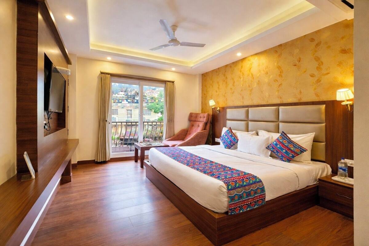 A hotel room with a bed, a chair, a TV, a ceiling fan, and a balcony with a view.