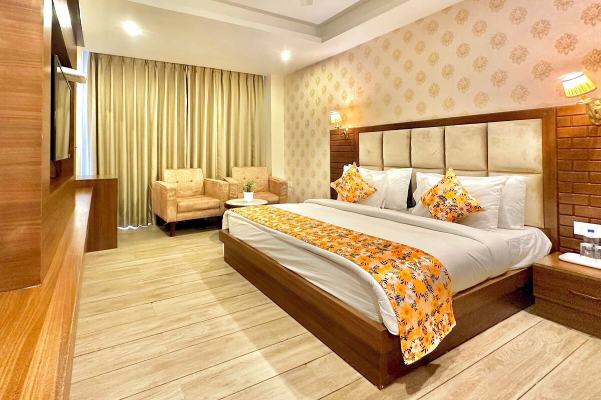A hotel room with a bed, two chairs, a small table, a ceiling fan, and a nightstand with a lamp.