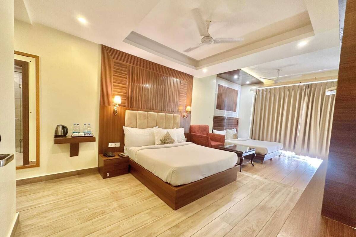 A hotel room with a large bed, a desk, a chair, a nightstand, a wall-mounted lamp, and a ceiling fan.
