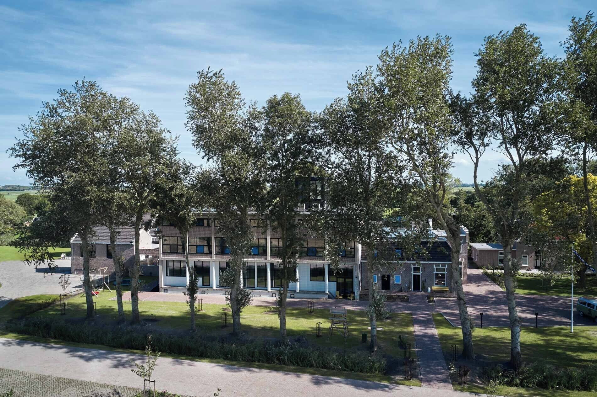 En byggnad med flera våningar, utformad i en modern arkitektonisk stil, omgiven av en välskött gräsmatta och träd.