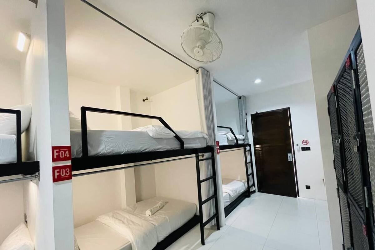 A dormitory room with bunk beds, a ceiling fan, and a door leading to another room.