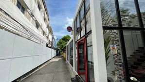 A narrow urban street with a modern building featuring large windows and a red door. - Samui Beach Hostel (Koh Samui)