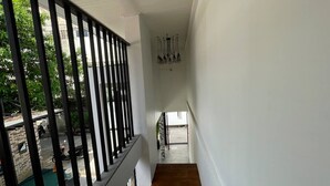 A staircase with a wooden handrail and black balusters leading to a landing with a view of the outside. - Samui Beach Hostel (Koh Samui)