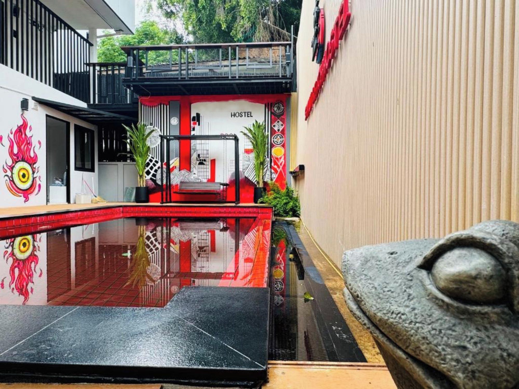 Um hostel com esquema de cores vermelho e branco, uma piscina pequena e uma escada que leva a um andar superior.