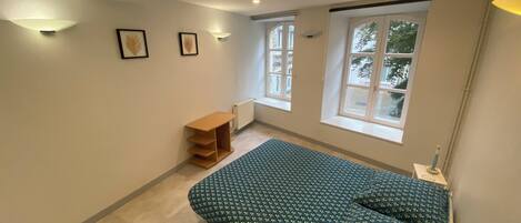 Un dormitorio con cama, ventana, radiador y estante.