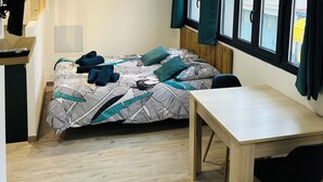 Ein kleines Zimmer mit Bett, Tisch und einem Vorhangfenster.