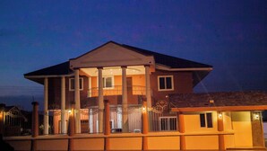 Une maison à deux étages dotée d’un balcon, de colonnes et d’une entrée fermée par un portail.