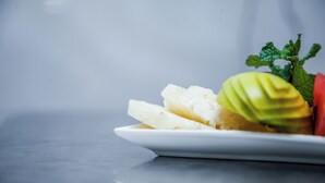 Une assiette de fruits coupés en tranches, décorée de quelques feuilles de menthe.
