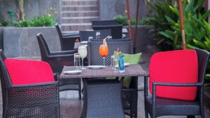 An outdoor dining area with wicker furniture and red cushions. - The Apartel Hotel  (Kumasi)