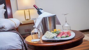 Une chambre d’hôtel avec un lit parfaitement fait, une table de chevet sur laquelle se trouvent une bouteille de vin, un verre à martini et une assiette de fruits.