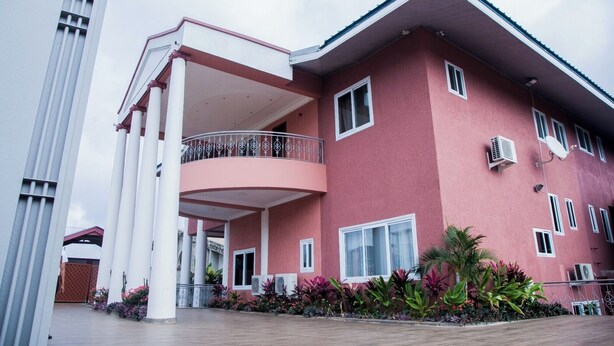 A multi-story building with a red facade, balconies, and air conditioning units. - The Apartel Hotel  (Kumasi)