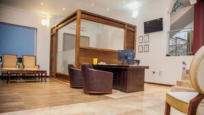 Un espace d’accueil comprenant un bureau en bois, deux fauteuils, une grande fenêtre et un escalier.