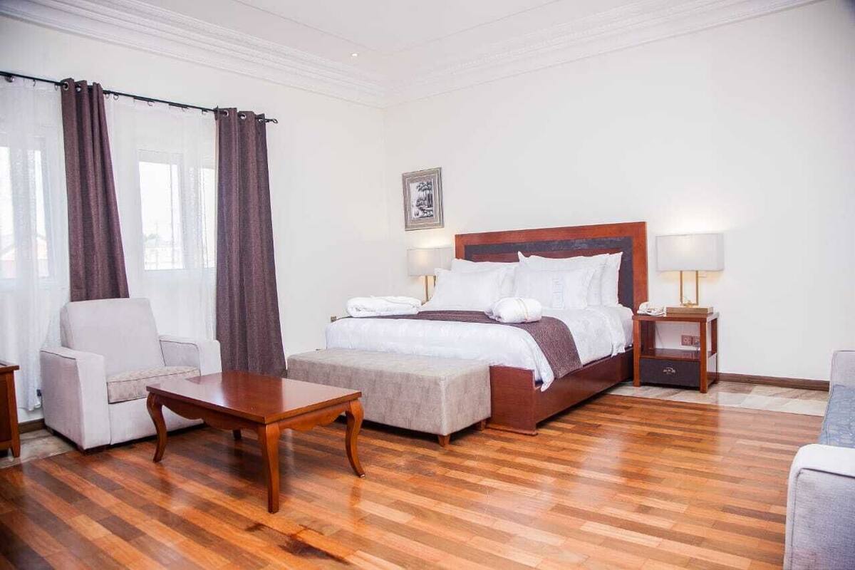 Une chambre d’hôtel avec un grand lit, un canapé, une petite table et une table de chevet avec une lampe.