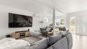 A modern living room with a large flat-screen TV, grey sofas, a white rug, and a wooden entertainment unit.