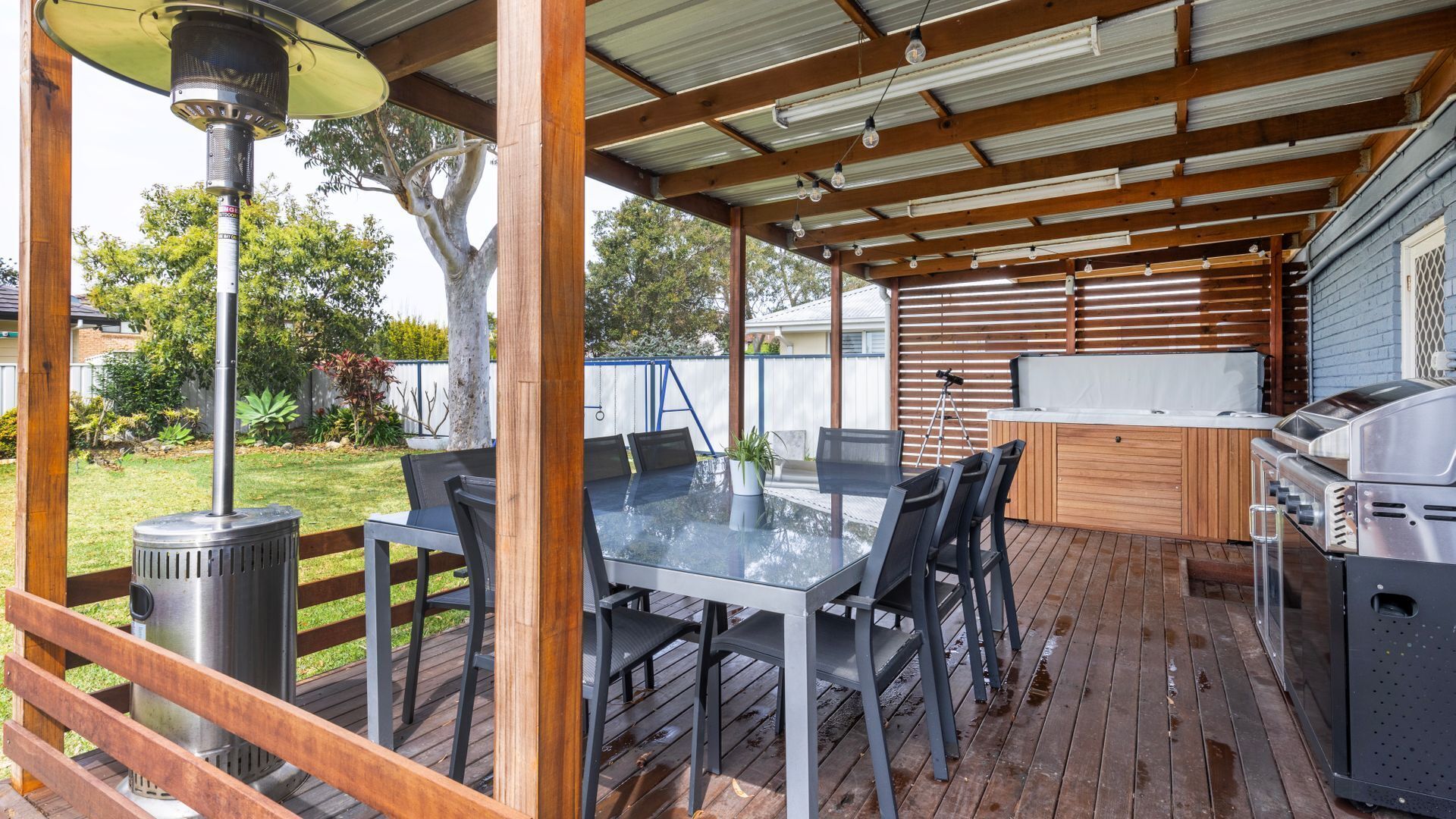 An outdoor patio with a glass table, chairs, a grill, and a pergola structure.
