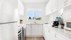A modern kitchen with white cabinets, a built-in oven, a sink, and a window with a view of trees.