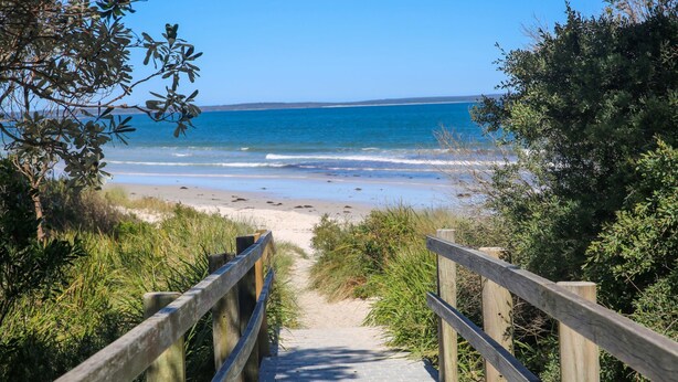 A wooden pathway leading to a beach with clear blue water and sandy shore.