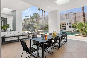 Une terrasse extérieure moderne, dotée d’une piscine, de coins salon et offrant une vue sur des palmiers et des montagnes.