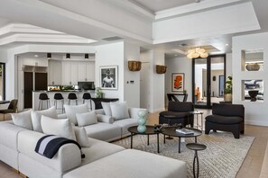 A modern living room with a sofa, armchairs, a coffee table, and a kitchen in the background.