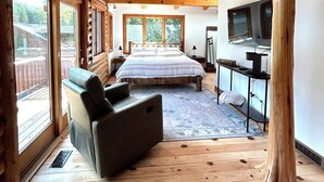 A log cabin bedroom with a large bed, a sofa, a ceiling fan, and a TV. - Custom River Front Property on 10 Acres, Sleeps 19 (Traverse City)