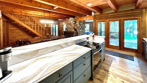 A spacious kitchen with a marble countertop, wooden ceiling beams, and a stone fireplace. - Custom River Front Property on 10 Acres, Sleeps 19 (Traverse City)