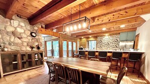 A rustic cabin interior with a stone wall, wooden dining table, and chairs. - Custom River Front Property on 10 Acres, Sleeps 19 (Traverse City)
