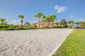 Ein Sandvolleyballfeld mit Netz, umgeben von Palmen und einem Spielplatz.
