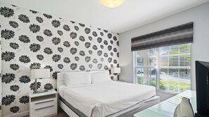 Un dormitorio moderno con una cama blanca, una mesita de noche, un escritorio y una ventana con persianas.