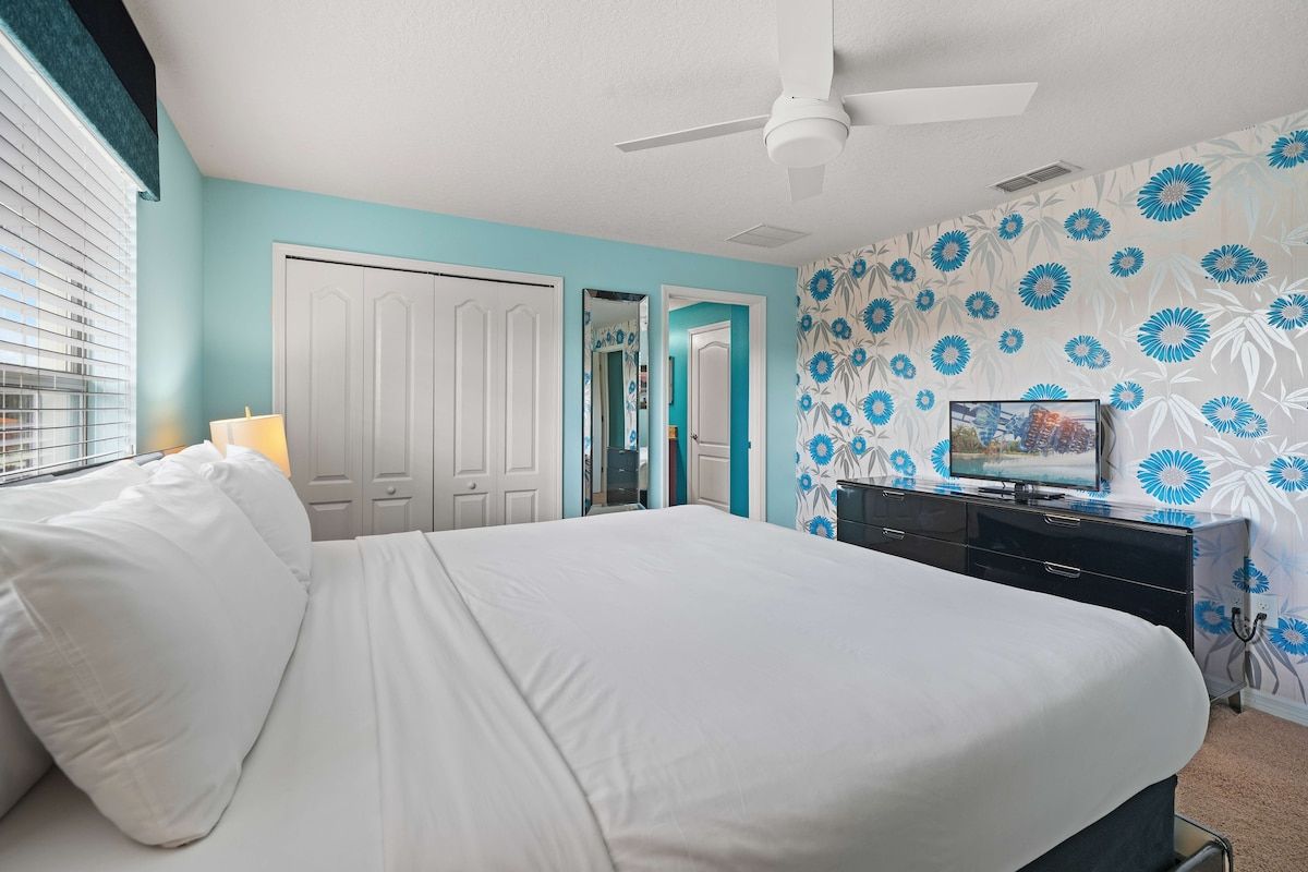 - Bright bedroom with a king-size bed, crisp white linens, and a bold turquoise floral accent wall - Large closet and sleek black dresser with a smart TV for added convenience - Spacious and airy with natural light highlighting the modern decor