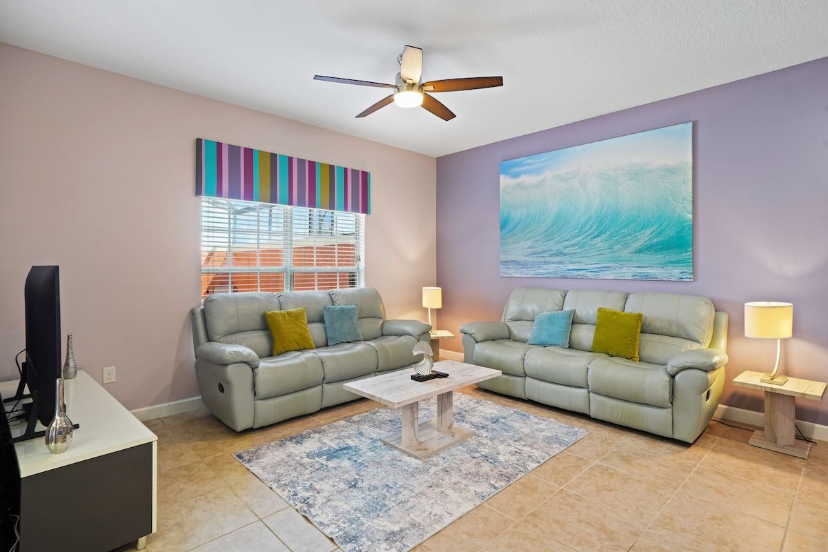 A living room with two sofas, a coffee table, a ceiling fan, a painting, and a window with blinds.