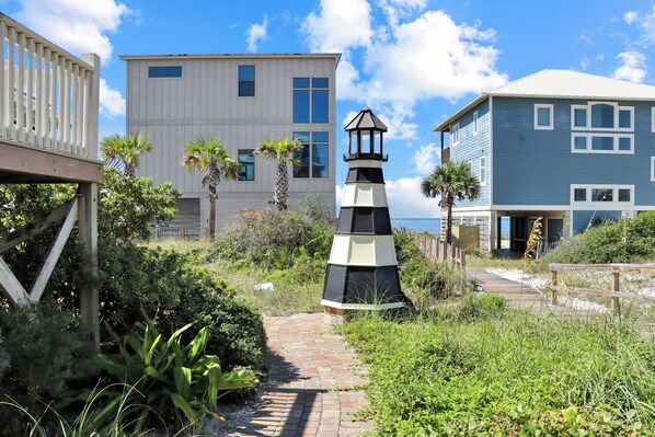 Um edifício costeiro com um farol, rodeado por vegetação exuberante e um calçadão de madeira.