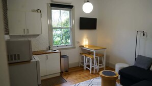Une cuisine compacte avec une fenêtre, un petit coin repas avec des tabourets, un canapé et une lampe.