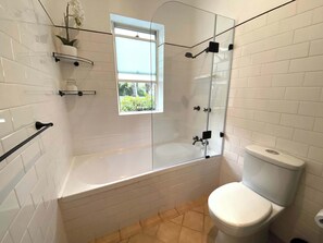 A bathroom with a glass-enclosed shower, a white toilet, and a window providing natural light.