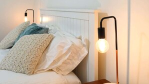 Une chambre à coucher avec un lit, des oreillers, une table de chevet, une lampe et deux tableaux accrochés au mur.
