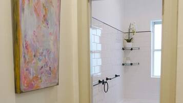 Une salle de bain avec des carreaux blancs, une douche, une porte en verre et un tableau au mur.