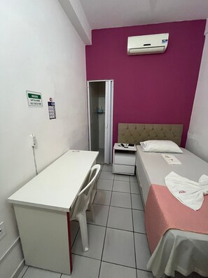 A small, clean room with a bed, a desk, and a chair. There is a white air conditioning unit on the wall and a door leading to another room. - POUSADA EXECUTIVA (Teresina)
